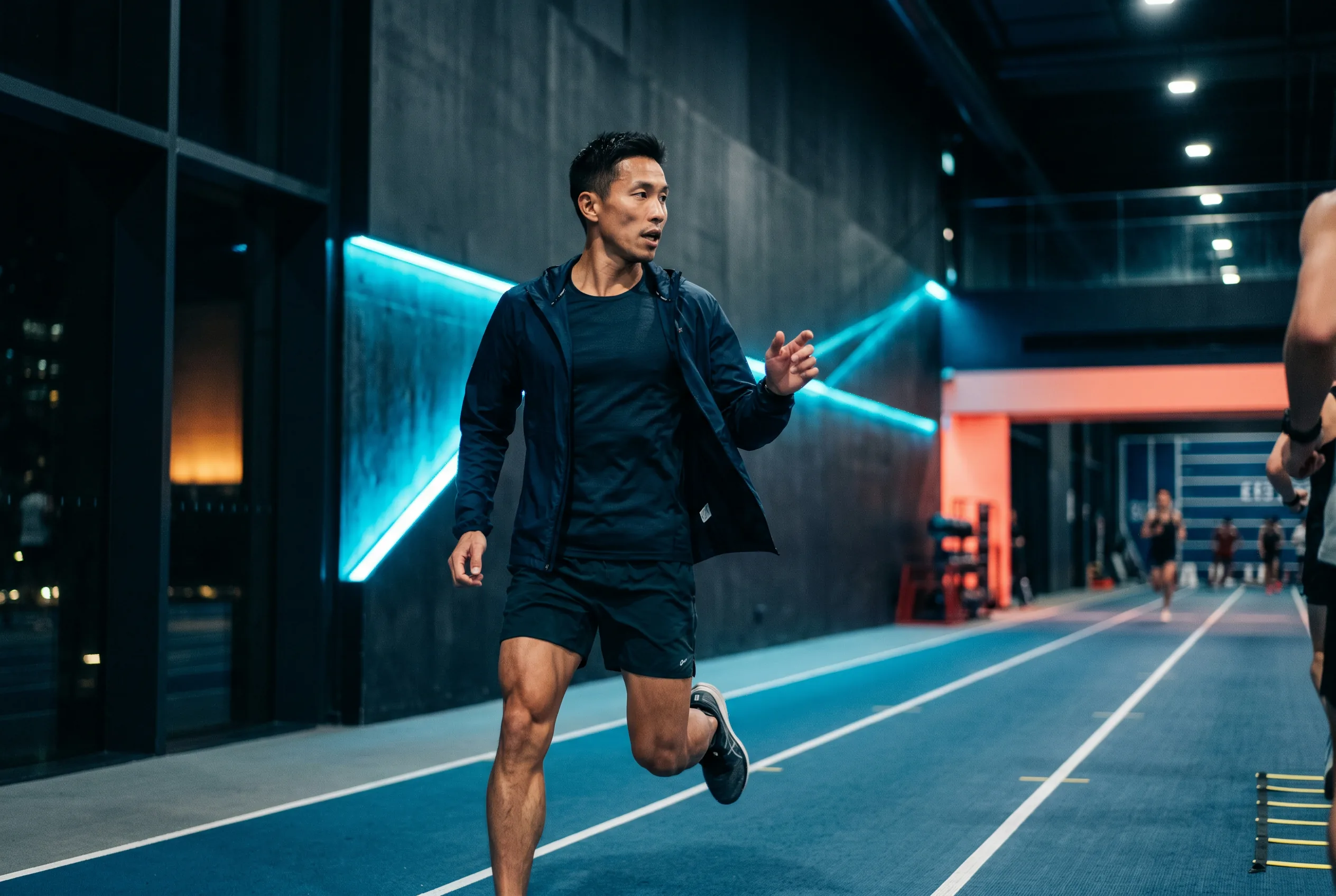 Coach Felix Tanaka running alongside athletes on the indoor lane